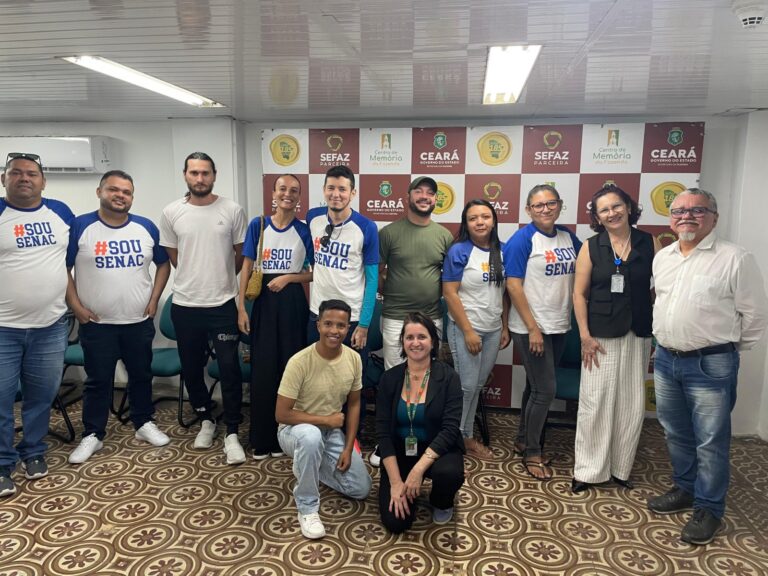 Foto de grupo com a professora Rosângela Xavier e alunos do Senac em frente a um banner institucional. A maioria das pessoas está sorrindo e algumas vestem camisetas com a inscrição "SOU SENAC". A foto é datada de 23 de julho.