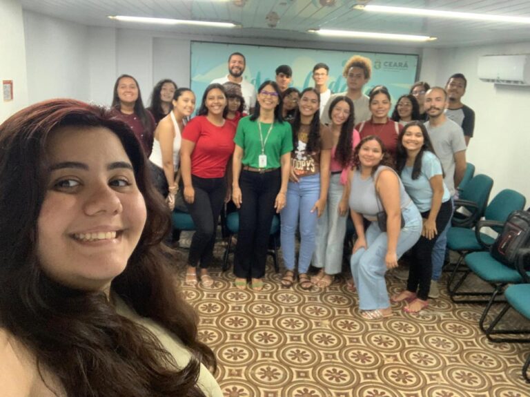 Uma foto em grupo de cerca de 20 pessoas, em um ambiente interno, capturada em 30 de julho. A foto é uma selfie, tirada por uma mulher sorridente em primeiro plano. O grupo inclui homens e mulheres de diversas idades, sorrindo para a câmera. Ao fundo, é possível ver um quadro com a palavra "Ceará". A foto celebra a visita do Conselho de Integração Social (Integrassol).