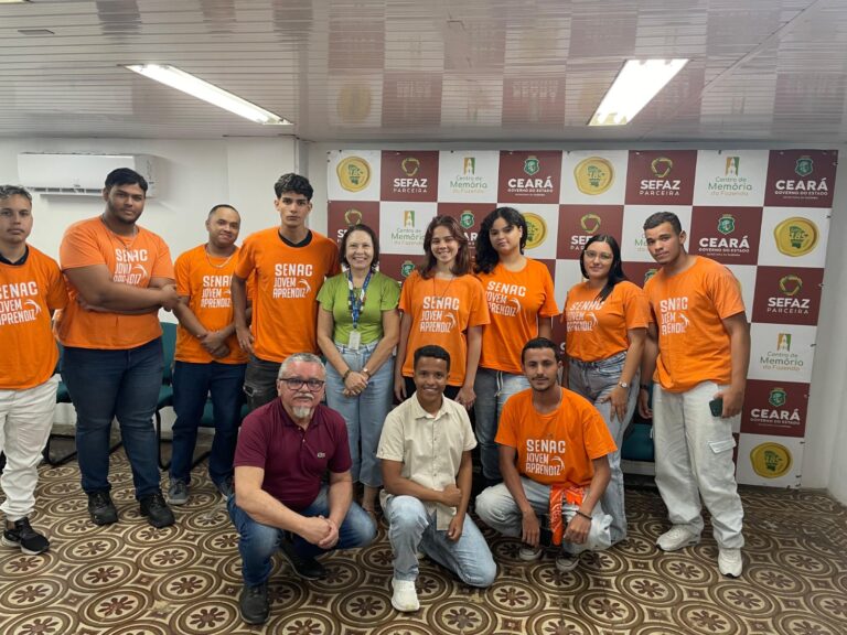 Foto de grupo com a professora Rosângela Xavier e alunos do Senac em frente a um banner institucional. A maioria das pessoas está sorrindo e usa camisetas laranjas. A foto é datada de 25 de julho.