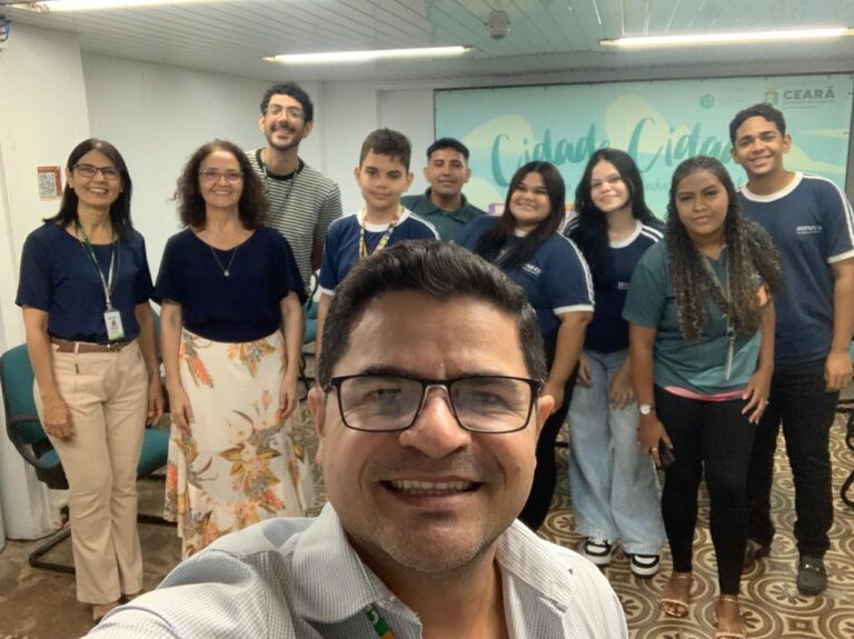 Selfie de um grupo em um ambiente interno, tirada na manhã de 6 de agosto. Na foto, estão seis jovens estagiários, acompanhados pelos servidores André Mendonça e Ruth Mourão. O grupo, que inclui três mulheres e cinco homens, está posando de forma amigável. A foto celebra o início do Projeto Jovens Estagiários da Sefaz. Um banner com a palavra "Ceará" e o logo da Sefaz é visível ao fundo.