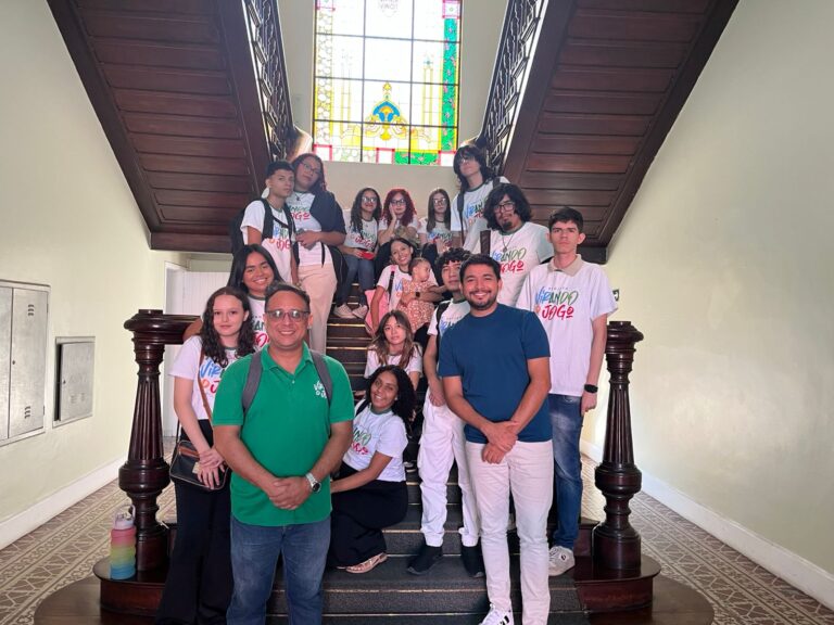 Grupo de alunos do projeto *Virando o Jogo* posando na escadaria da Sefaz-CE durante visita em 26 de setembro, com dois educadores à frente e um vitral colorido ao fundo.