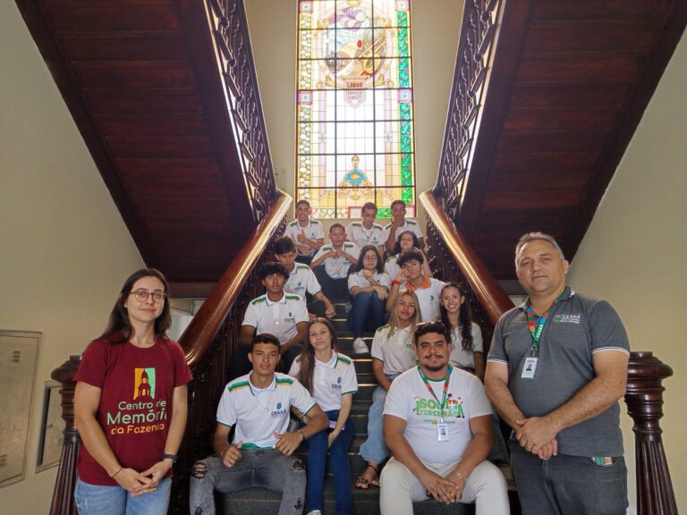 Treze alunos e dois professores (Francisco de Assis e Thiago Amorim) do EEMTI Raul Tavares Cavalcante de Itaitinga, posando em uma sala de treinamento da SEFAZ, com muitos alunos vestindo camisetas brancas e verdes.