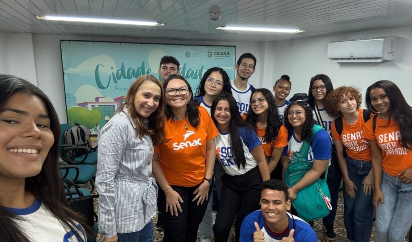 Grupo de 14 alunos do curso de Auxiliar Administrativo, acompanhados pela professora Cristiane, visitando o Centro de Memória da Fazenda. Os visitantes estão observando uma exposição ou atividade no espaço, com algumas cadeiras e elementos expositivos visíveis ao fundo