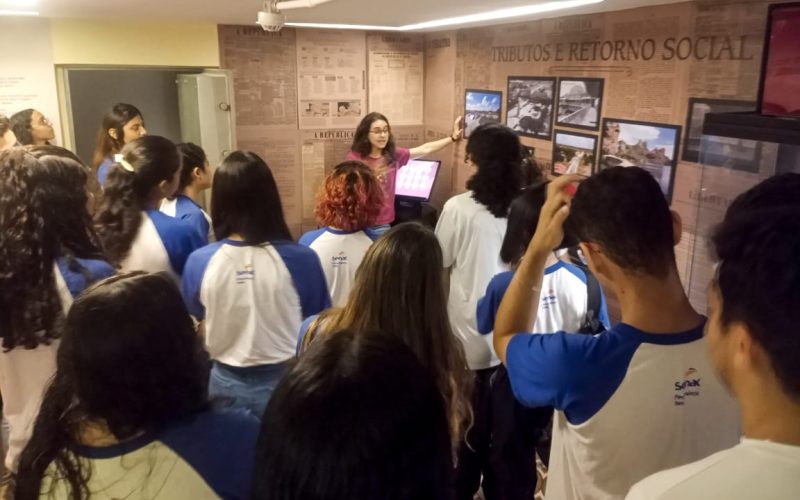 Visita do grupo de estudantes do Serviço Nacional de Aprendizagem Comercial (Senac) Ceará, no dia 29 de Maio. As visitas fazem parte do projeto Escola no Fisco, idealizado pelo Programa de Educação Fiscal (PEF-CE), com o objetivo de convidar estudantes para conhecerem as atividades desenvolvidas pela Secretaria da Fazenda do Ceará (Sefaz-CE) e refletirem sobre tributação e cidadania. Foto: estudantes na exposição “Notas de Memória” do Centro de Memória da Secretaria da Fazenda do Ceará.