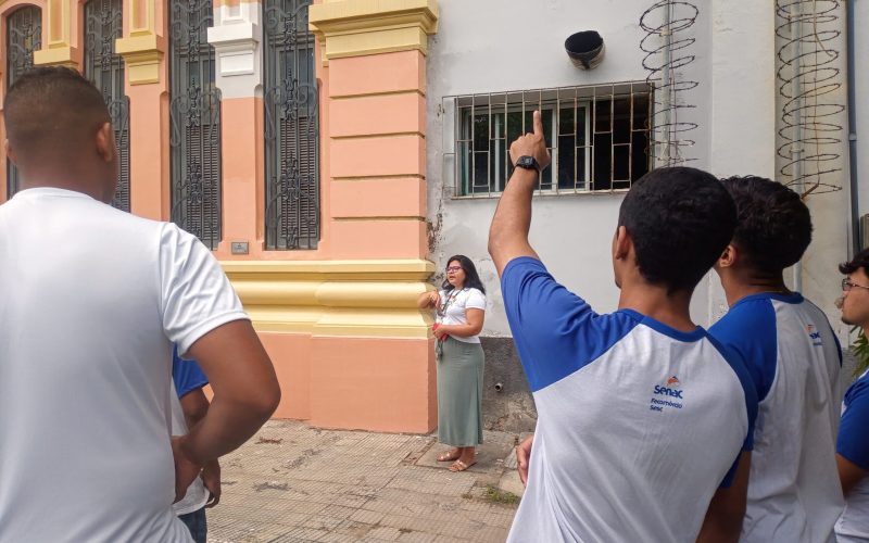 Visita do grupo de estudantes do Serviço Nacional de Aprendizagem Comercial (Senac) Ceará, no dia 30 de Junho. As visitas fazem parte do projeto Escola no Fisco, idealizado pelo Programa de Educação Fiscal (PEF-CE), com o objetivo de convidar estudantes para conhecerem as atividades desenvolvidas pela Secretaria da Fazenda do Ceará (Sefaz-CE) e refletirem sobre tributação e cidadania. Foto: estudantes no momento da visita a “Janela Testemunho” na fachada do Centro de Memória da Secretaria da Fazenda do Ceará.